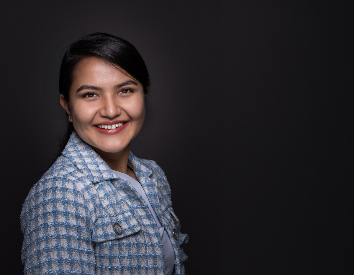 Professional portrait in a blue checked jacket against a dark studio background.