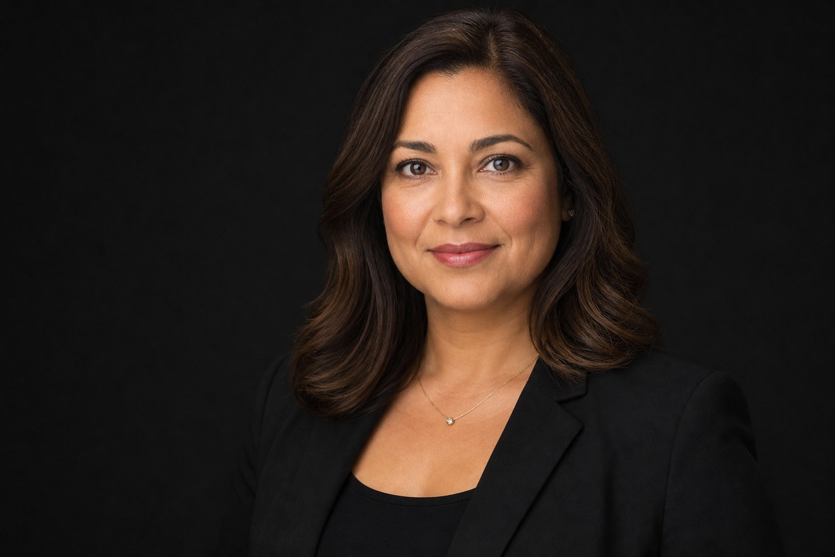 Professional headshot in a black blazer against a dark studio background.