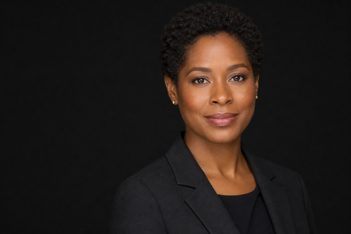 Professional headshot in a black blazer against a dark studio background.